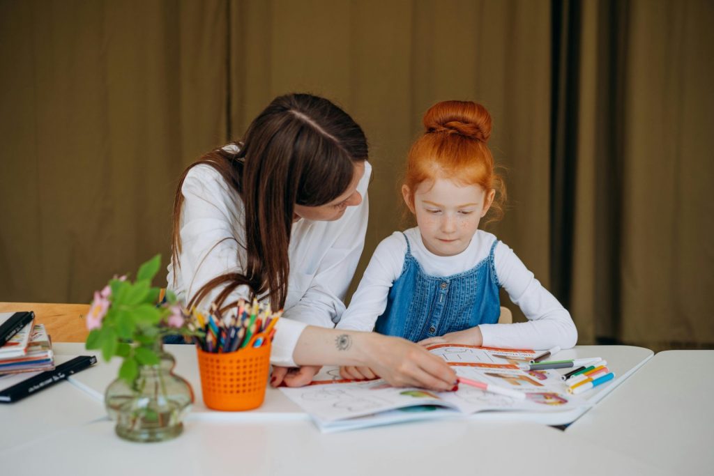 Eine Lehrerin unterstützt ein junges Mädchen bei einer Lernaktivität im Klassenzimmer und fördert so die Bildung.